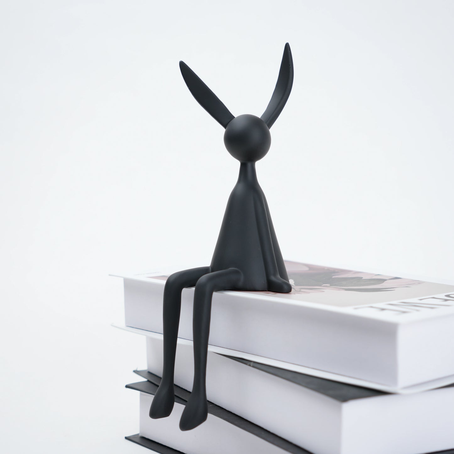 Black rabbit-shaped bookend on a stack of books with a white background