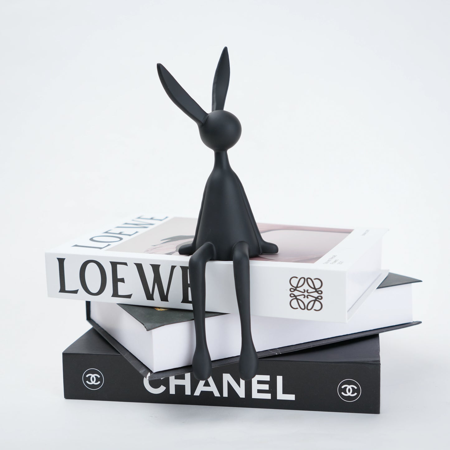 Black rabbit sculpture on top of Chanel and Loewe boxes with a white background