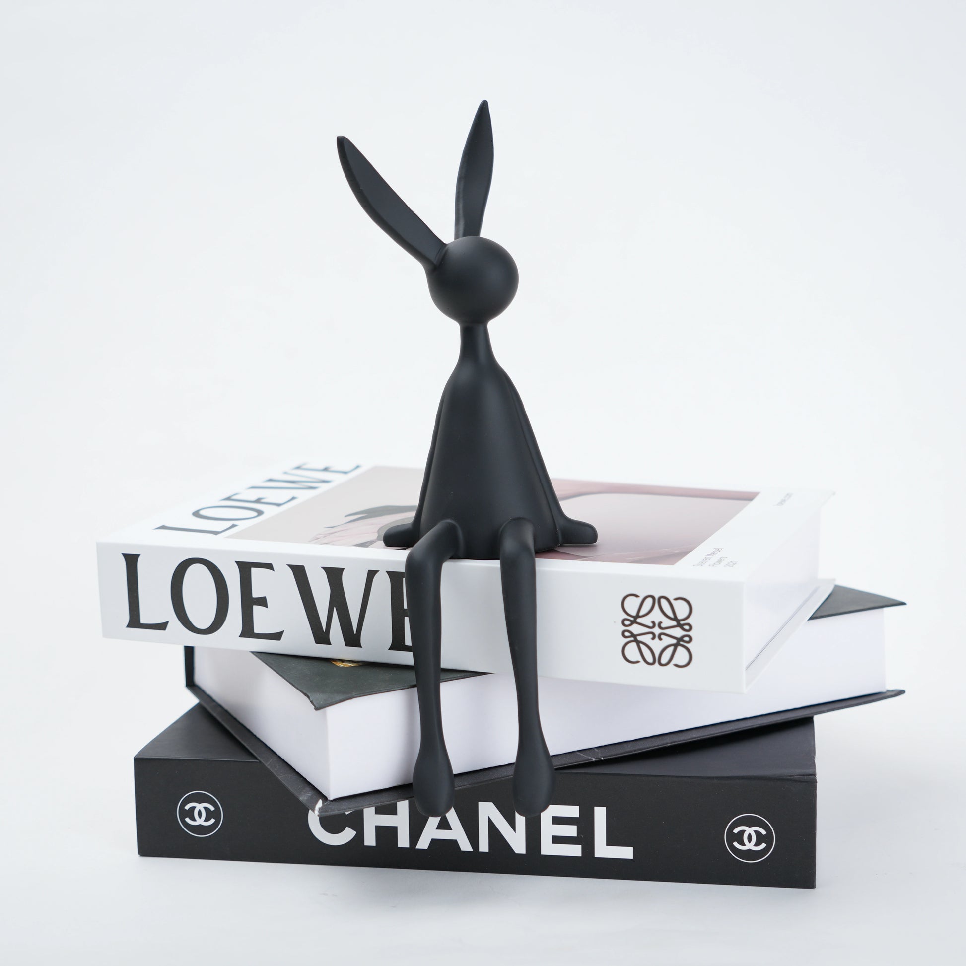Black rabbit sculpture on top of Chanel and Loewe boxes with a white background