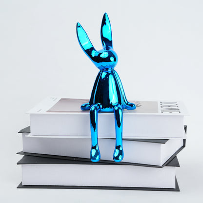 Resin bunny figurine with elongated ears and a minimal seated design, featuring smooth contours and extended legs for edge placement, available in matte and reflective electroplated finishes.