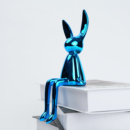 Blue metallic rabbit sculpture on a white surface with a light gray background
