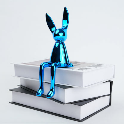 Blue metallic rabbit figurine sitting on a stack of books against a white background