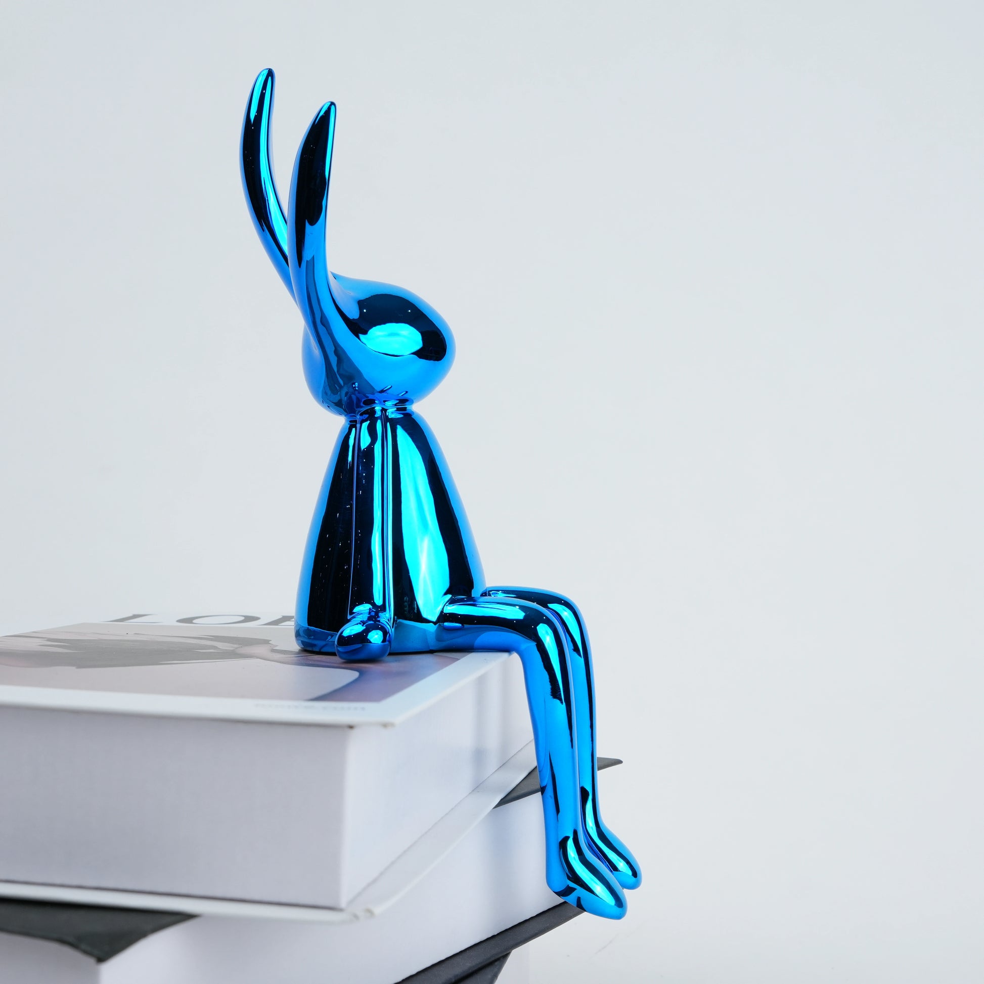 Shiny blue rabbit sculpture on a white surface with a light gray background