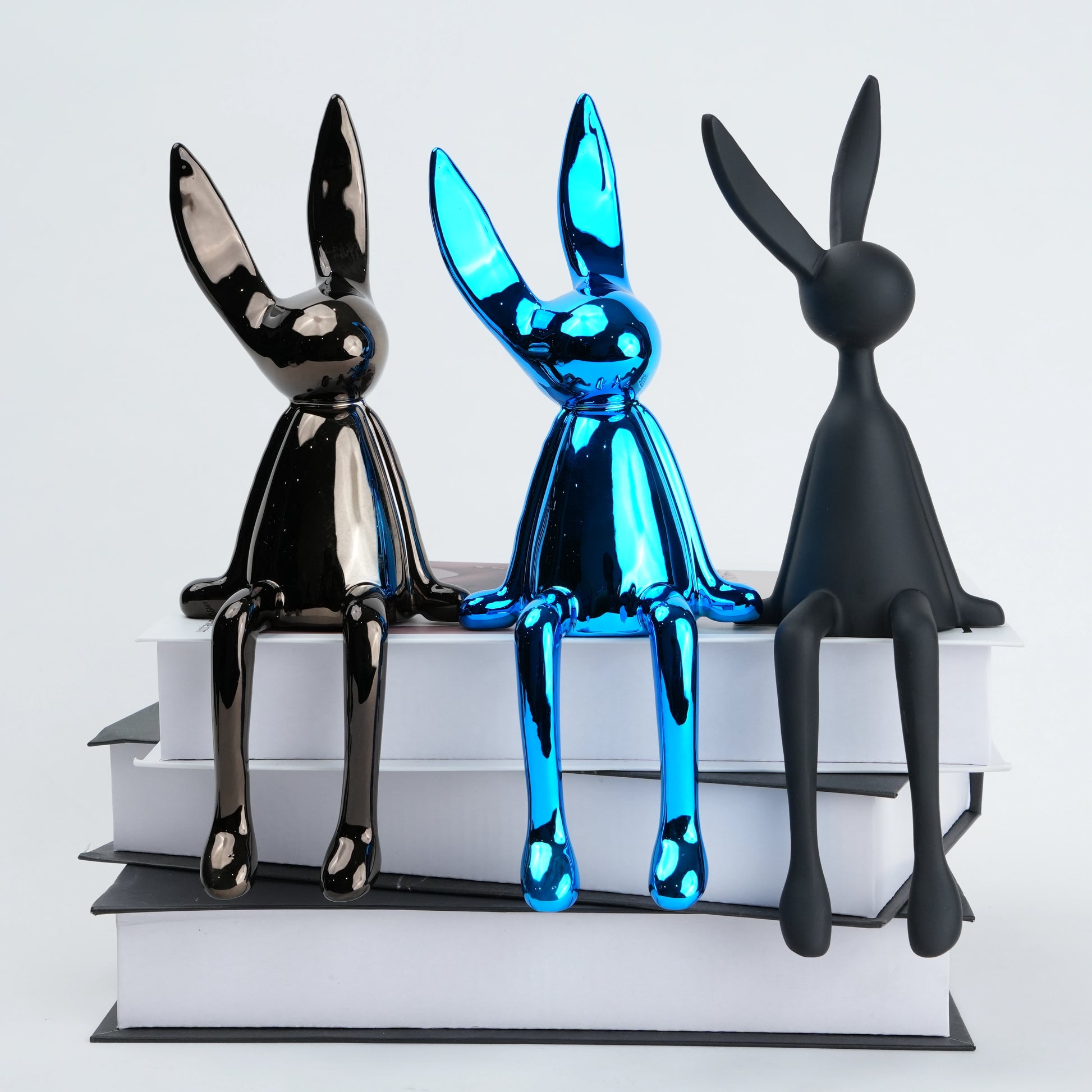 Resin bunny figurine with elongated ears and a minimal seated design, featuring smooth contours and extended legs for edge placement, available in matte and reflective electroplated finishes.