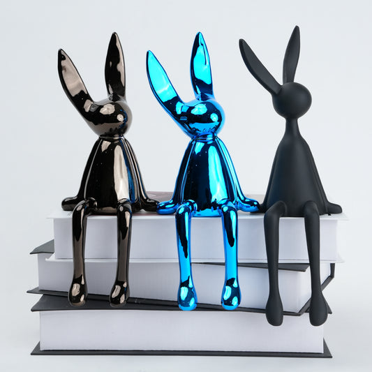 Resin bunny figurine with elongated ears and a minimal seated design, featuring smooth contours and extended legs for edge placement, available in matte and reflective electroplated finishes.
