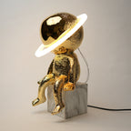 Gold astronaut lamp with a white light on a gray background