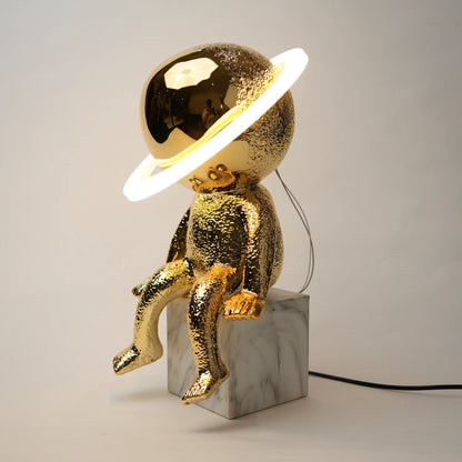 Gold astronaut lamp with a white light on a gray background
