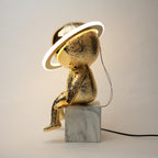 Gold sculpture with a lamp on a marble base against a plain background