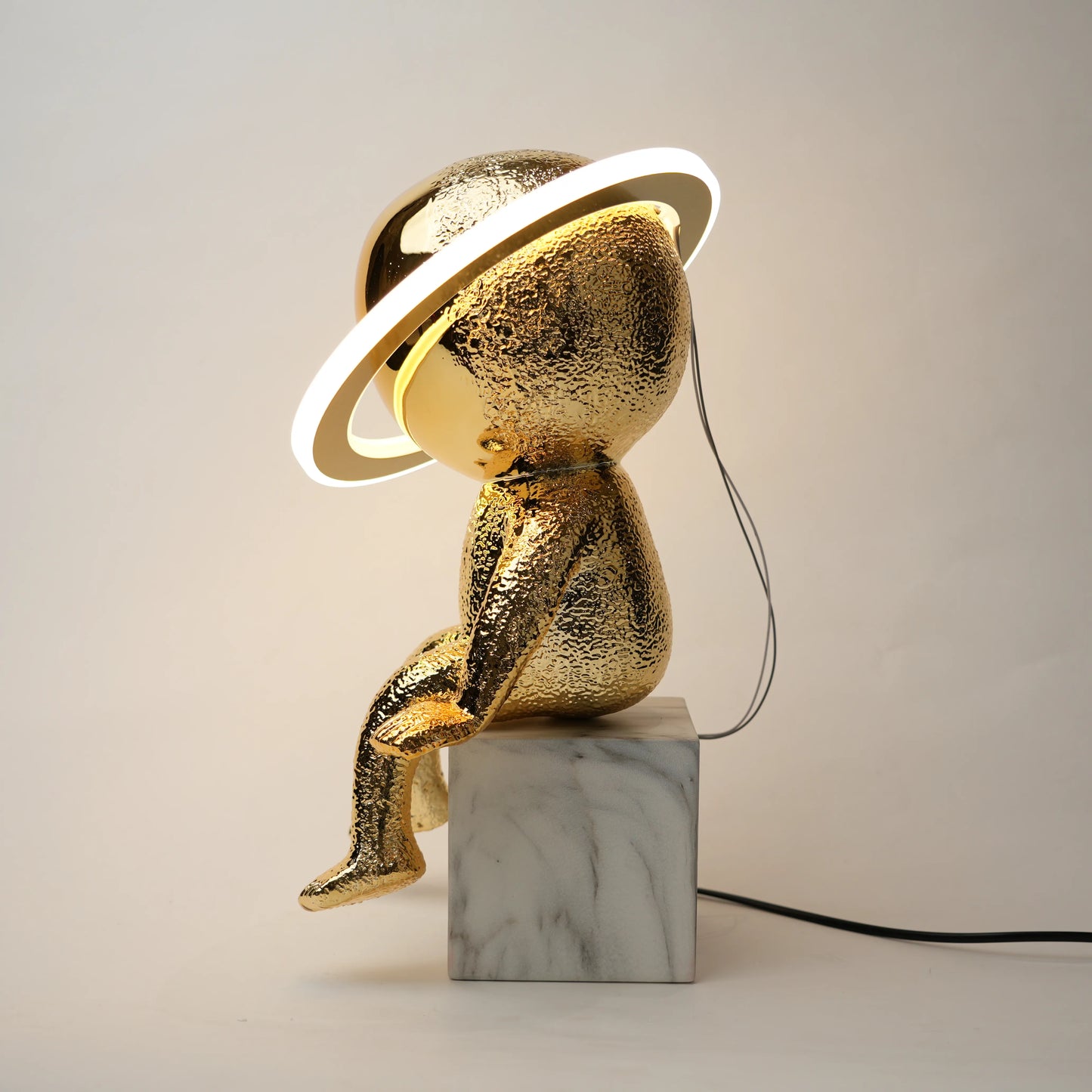 Gold sculpture with a lamp on a marble base against a plain background