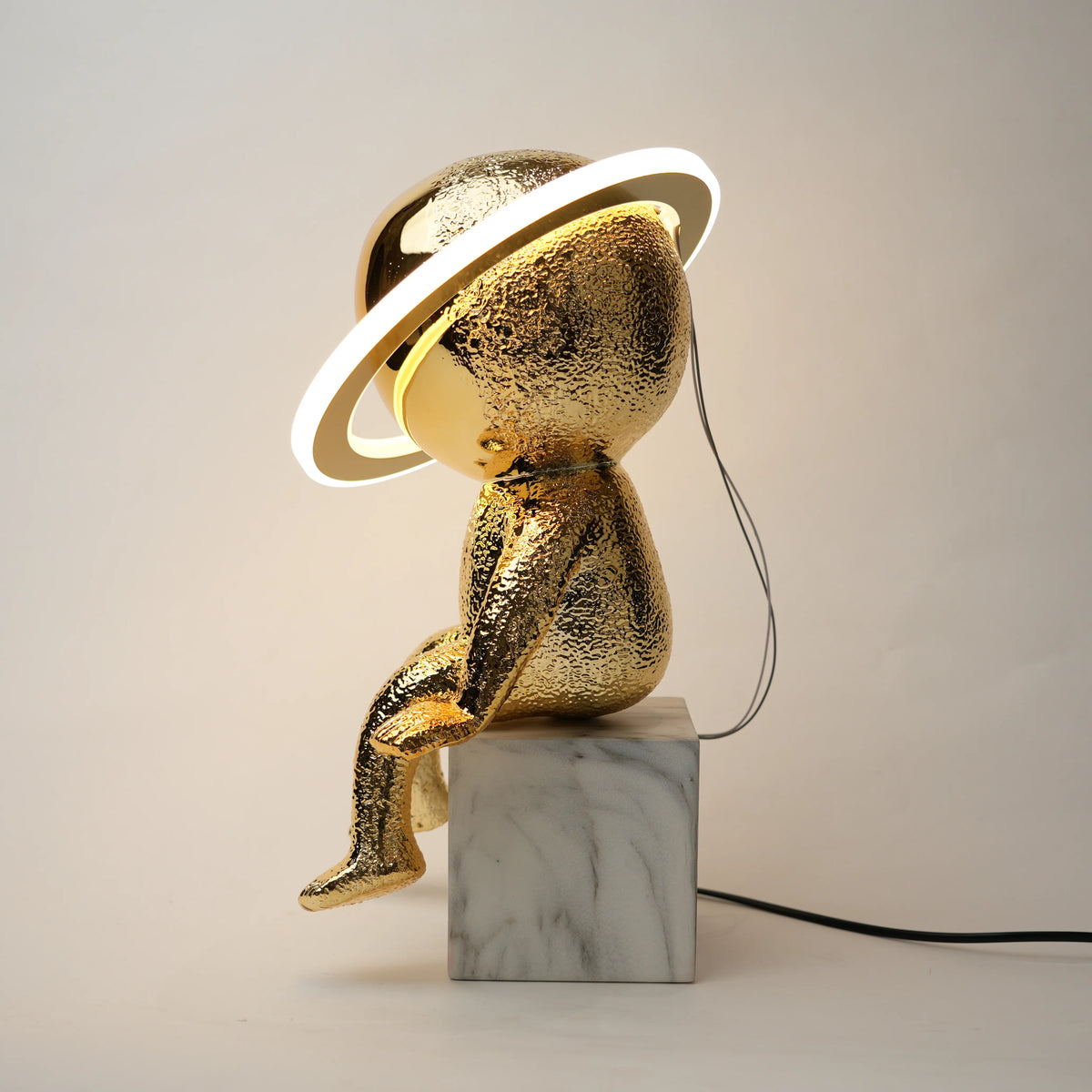 Gold sculpture with a lamp on a marble base against a plain background