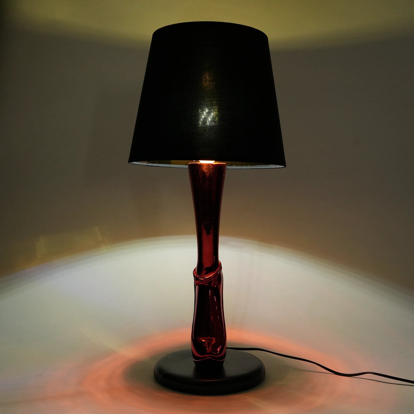 Table lamp with black shade and red base on a neutral background