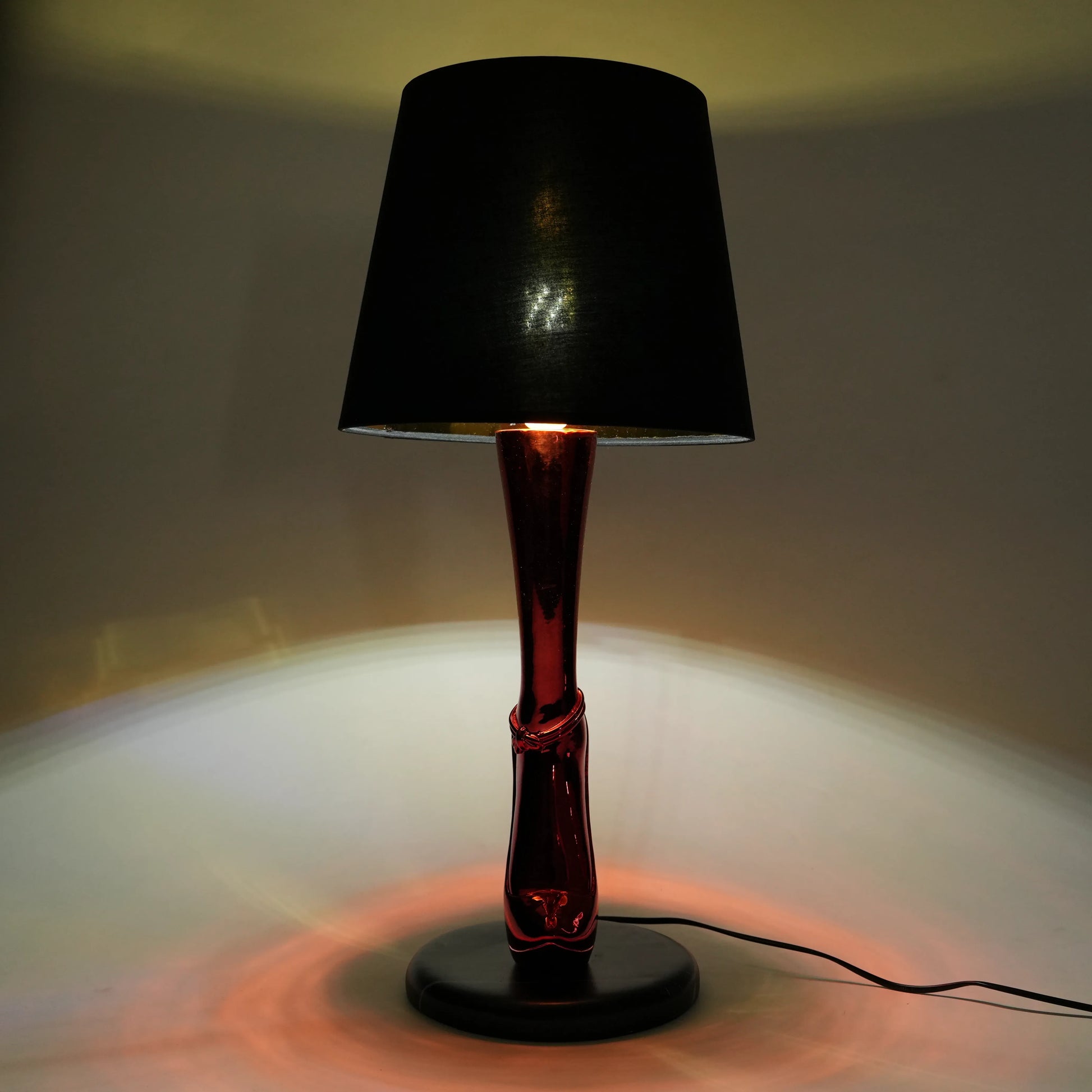 Table lamp with black shade and red base on a neutral background