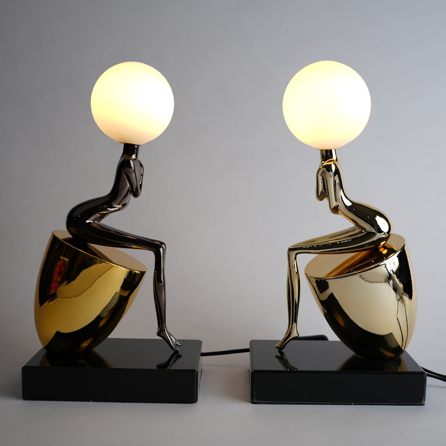 Two artistic table lamps with gold and black bases on a gray background