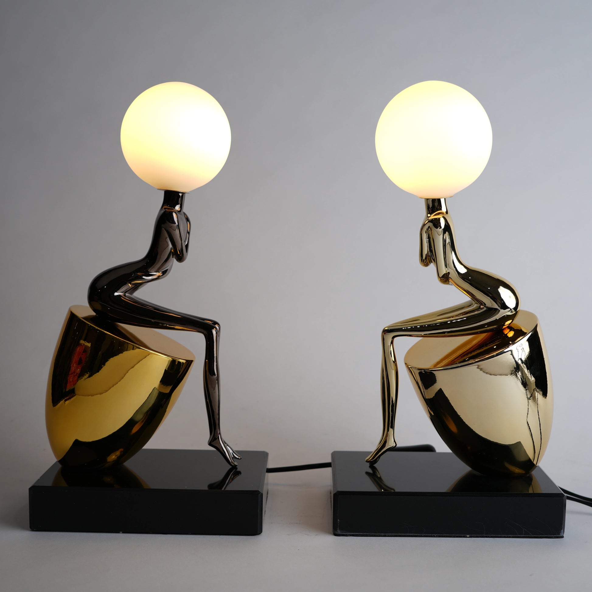 Two artistic table lamps with gold and black bases on a gray background