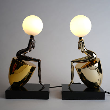 Two artistic table lamps with gold and black bases on a gray background