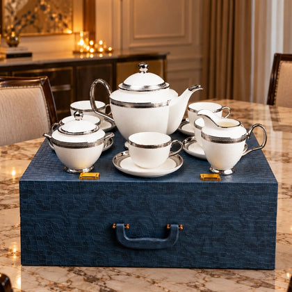 Six white ceramic espresso cups with matching saucers, each accented with a polished silver rim, arranged in a circular pattern on a dark gray background.