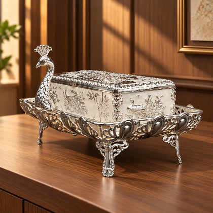 An ornate sterling silver decorative box with a peacock-shaped lid and matching footed base, photographed on a dark studio background.