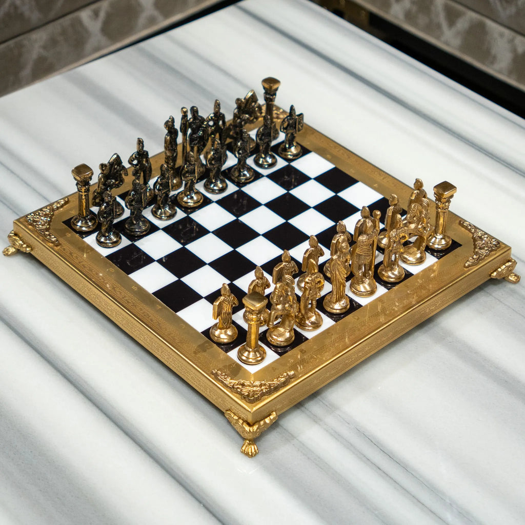 A close-up of ornate gold chess pieces arranged on a glossy black-and-white checkered board with a gold frame, photographed in a real indoor setting with a blurred sofa and pillow in the background.