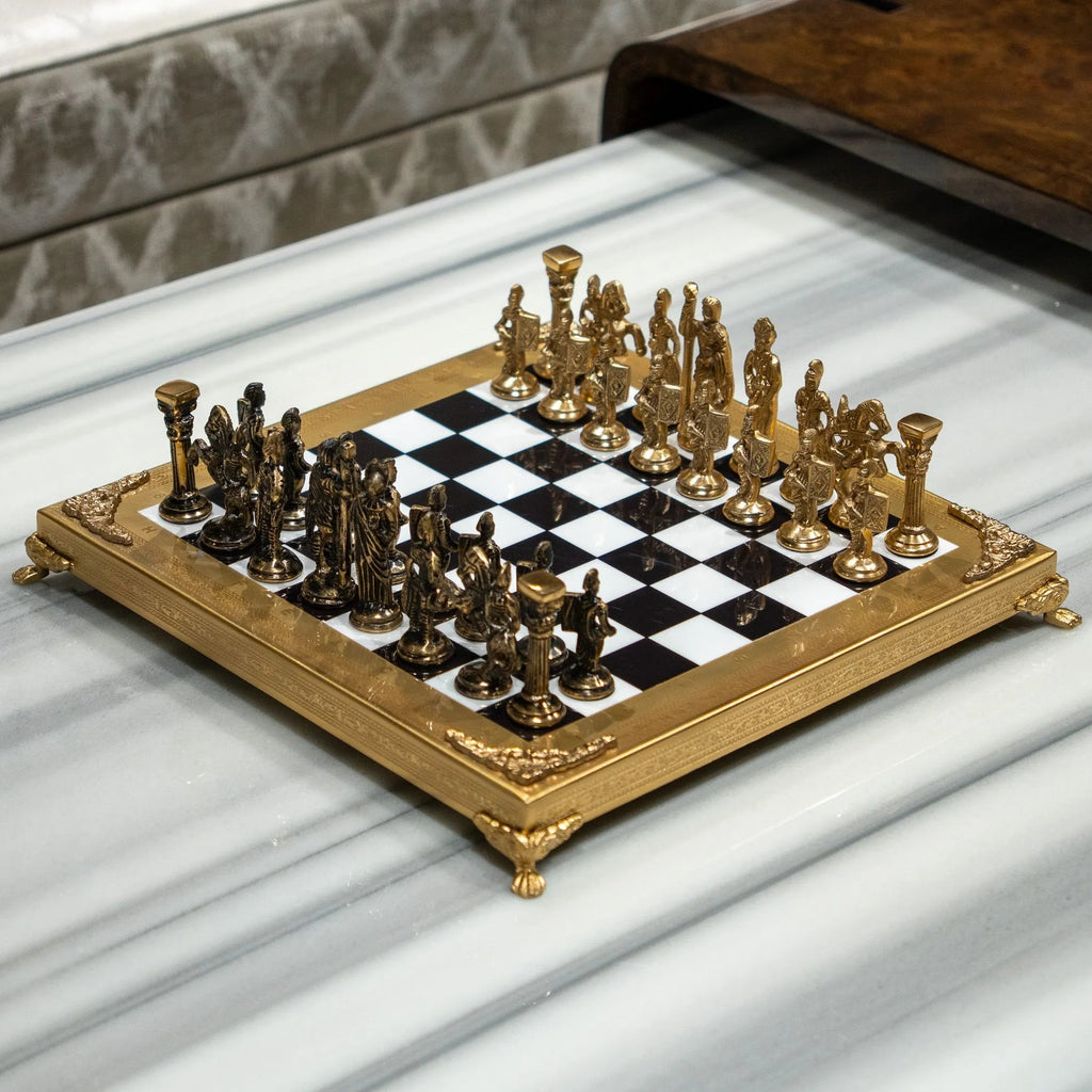 An ornate chess set with a gold-plated frame and metallic gold and bronze figurines, arranged on a black and white checkered board over a white marble surface.