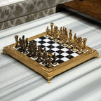 An ornate chess set with a gold-plated frame and metallic gold and bronze figurines, arranged on a black and white checkered board over a white marble surface.