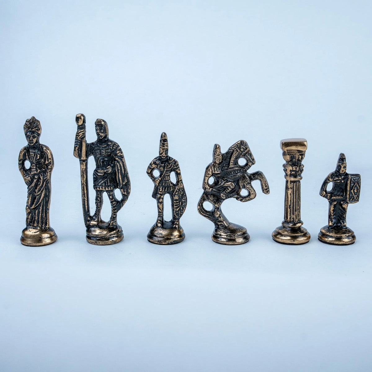Six small metallic figurines resembling ancient or classical game pieces arranged in a row on a light blue background.