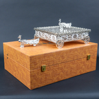 Silver decorative miniature horse-drawn chariot showpiece featuring an intricately detailed rectangular carriage with ornate embossed floral patterns, a transparent reflective top, decorative silver horse figurines, and four beautifully designed ornamental wheels. An elegant luxury home décor accent for tabletops, living rooms, display shelves and premium interiors.