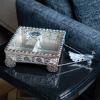 Silver decorative miniature horse-drawn chariot showpiece featuring an intricately detailed rectangular carriage with ornate embossed floral patterns, a transparent reflective top, decorative silver horse figurines, and four beautifully designed ornamental wheels. An elegant luxury home décor accent for tabletops, living rooms, display shelves and premium interiors.