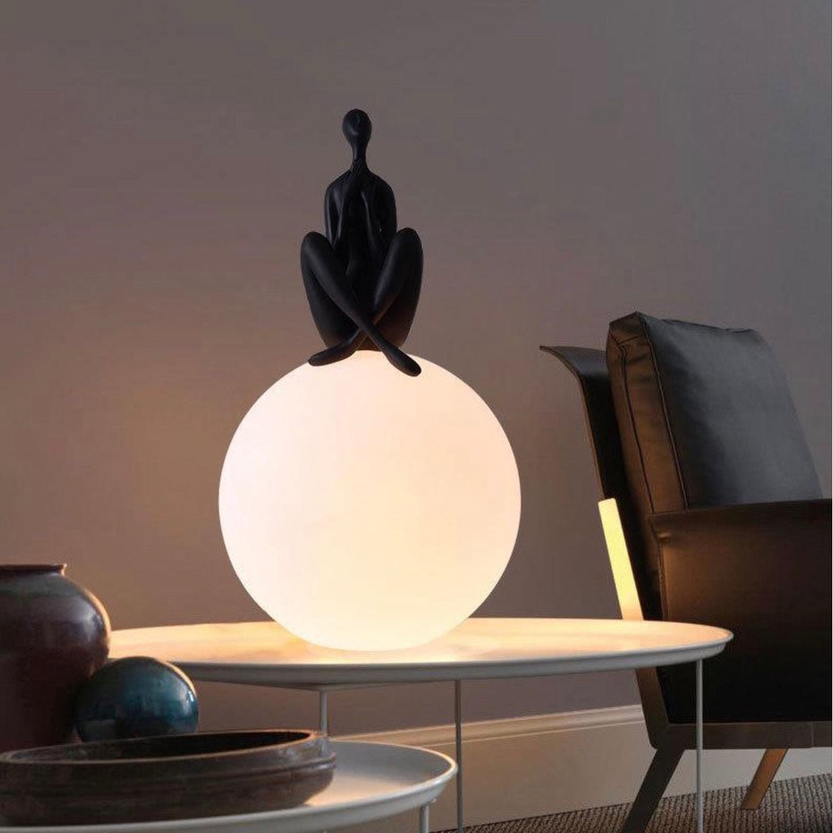 Black human sculpture seated on glowing sphere – Glow Contemplation Lamp