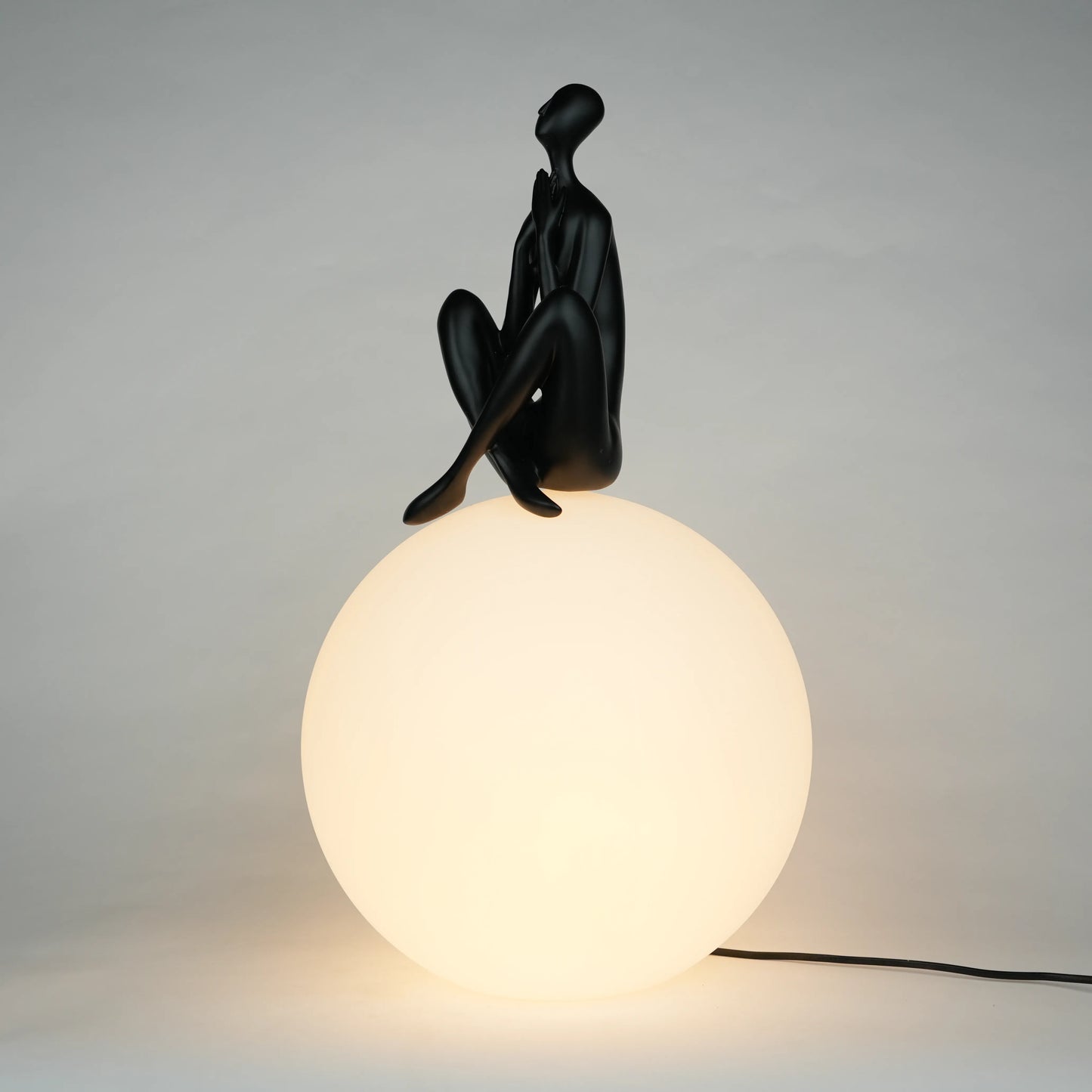 Black human sculpture seated on glowing sphere – Glow Contemplation Lamp