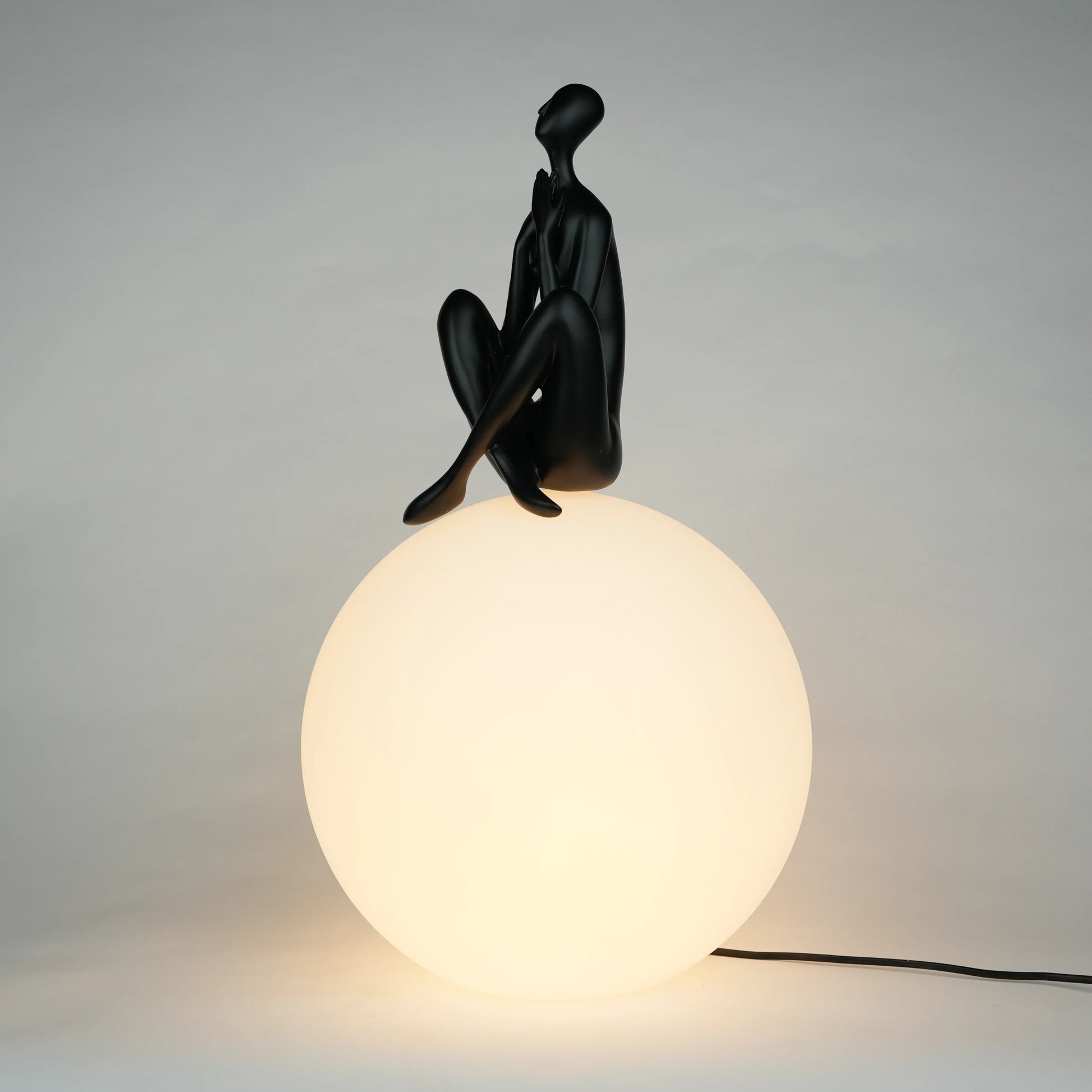 Black human sculpture seated on glowing sphere – Glow Contemplation Lamp