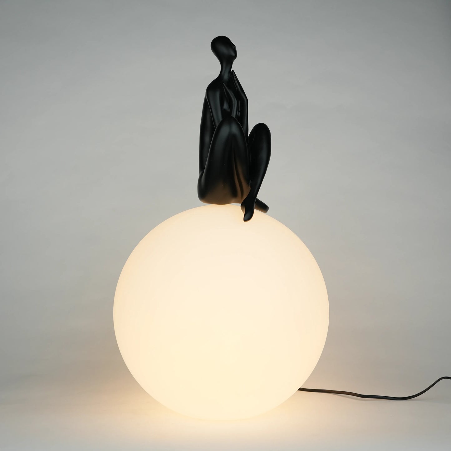 Black human sculpture seated on glowing sphere – Glow Contemplation Lamp