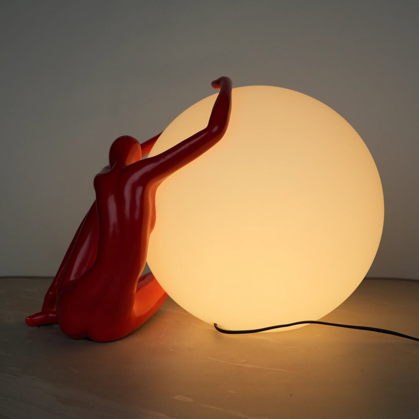 Crimson Embrace Lamp – Glossy red sculptural figure embracing a glowing orb – modern artistic table lamp by Ghar Art.