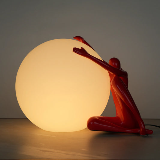 Crimson Embrace Lamp – Glossy red sculptural figure embracing a glowing orb – modern artistic table lamp by Ghar Art.