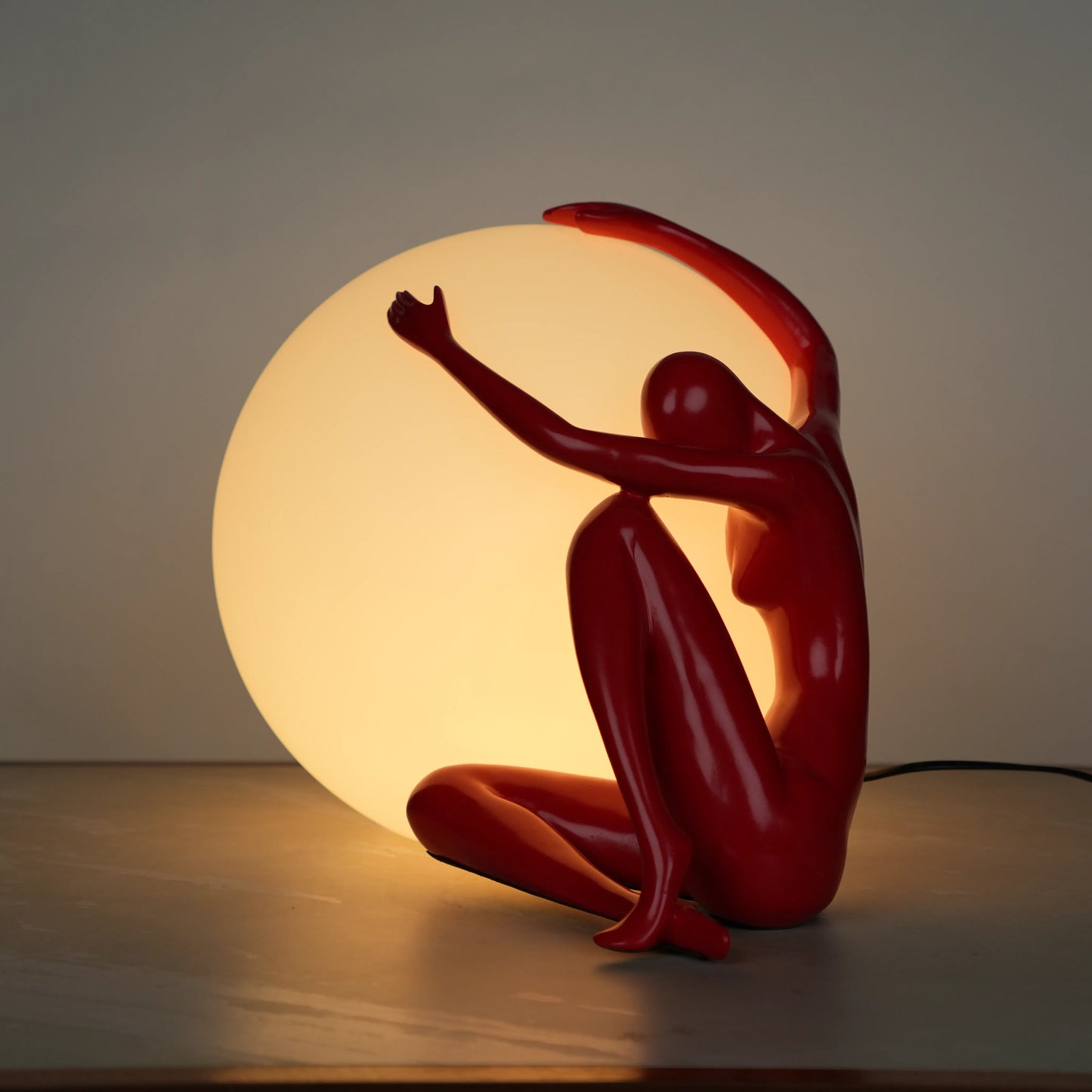 Crimson Embrace Lamp – Glossy red sculptural figure embracing a glowing orb – modern artistic table lamp by Ghar Art.