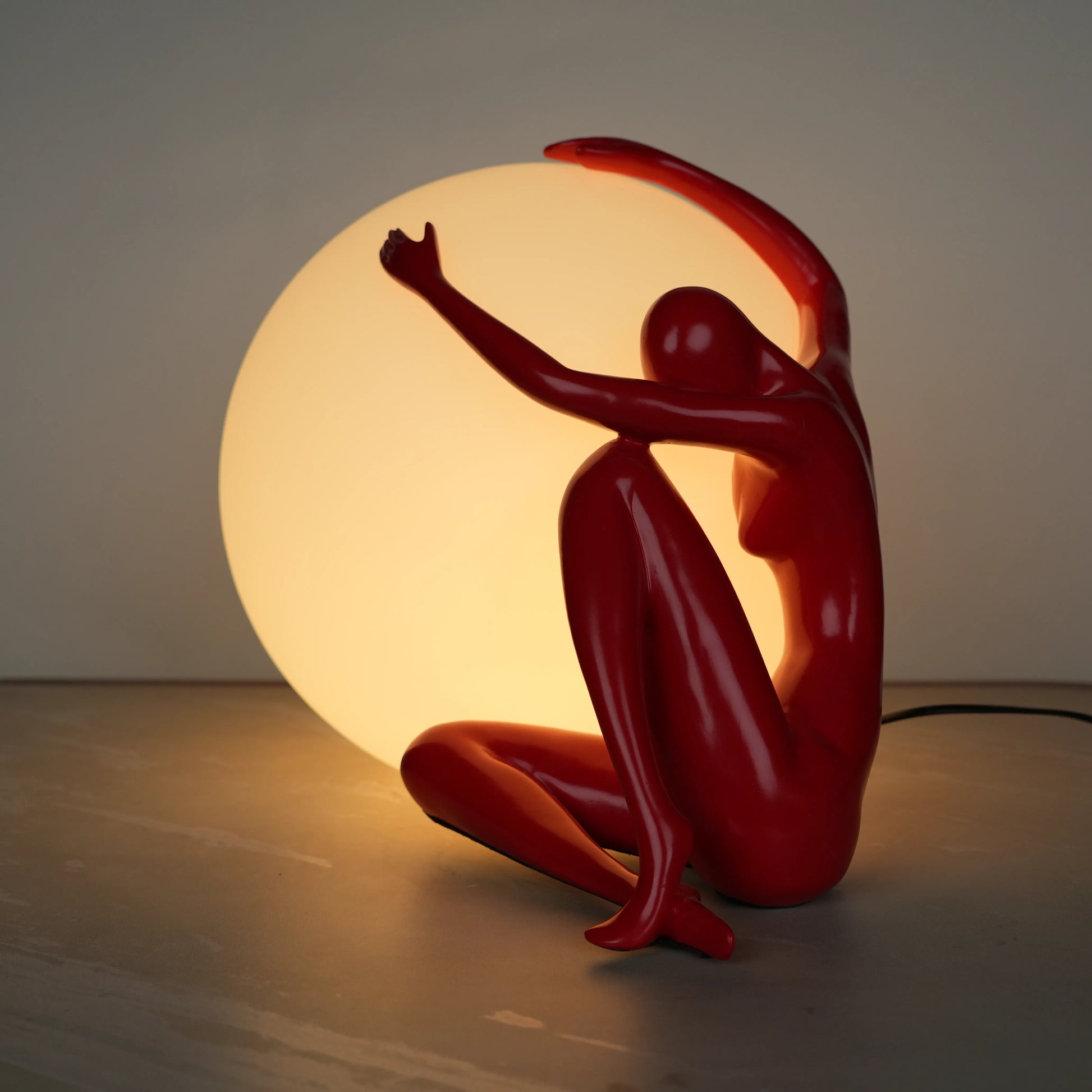 Crimson Embrace Lamp – Glossy red sculptural figure embracing a glowing orb – modern artistic table lamp by Ghar Art.