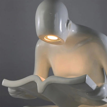 Glossy white reading sculpture lamp with abstract seated figure holding a book and built-in LED light.