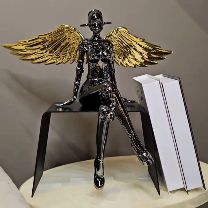 Chrome angel figurine with gold wings seated in a modern pose.