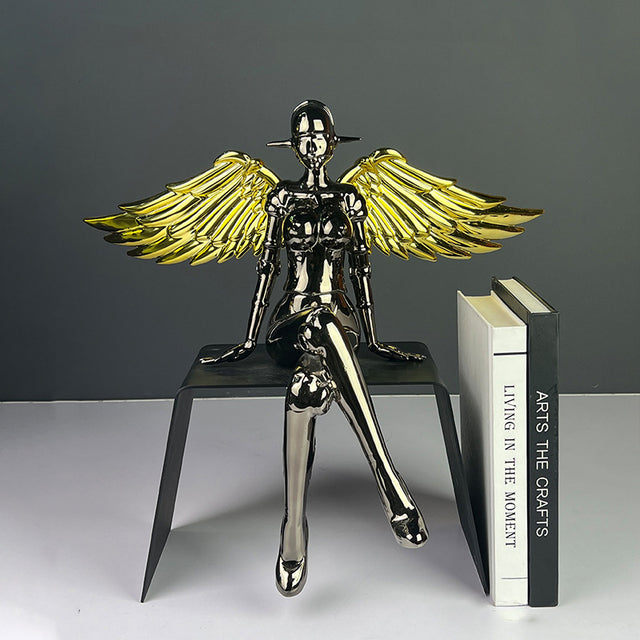 Chrome angel figurine with gold wings seated in a modern pose.