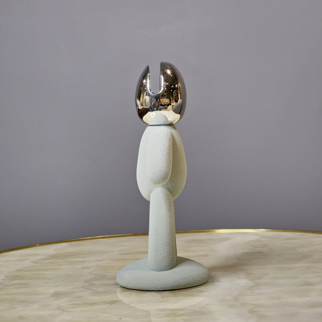 Minimalist human form decor object with textured surface and chrome head.