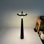 Modern cordless LED table lamp featuring a minimalist black conical base and floating circular shade, designed for ambient lighting in bedrooms, living rooms, offices, cafés and contemporary interiors.