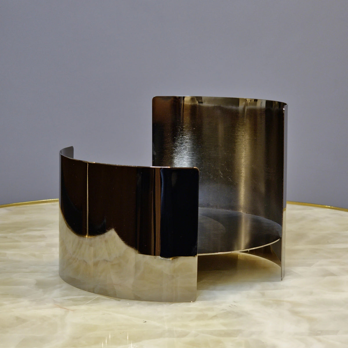 Contemporary metallic pedestal stand with curved design and reflective finish.