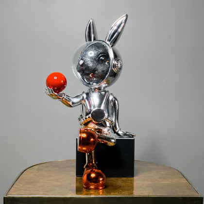 metallic rabbit figurine sculpture holding red sphere with reflective chrome finish, modern character decor for luxury tabletop, console and shelf styling