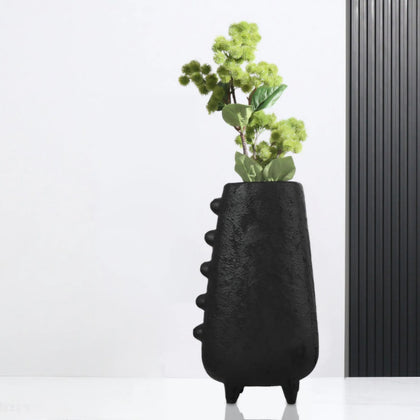 Black textured vase with green plant against a white background
