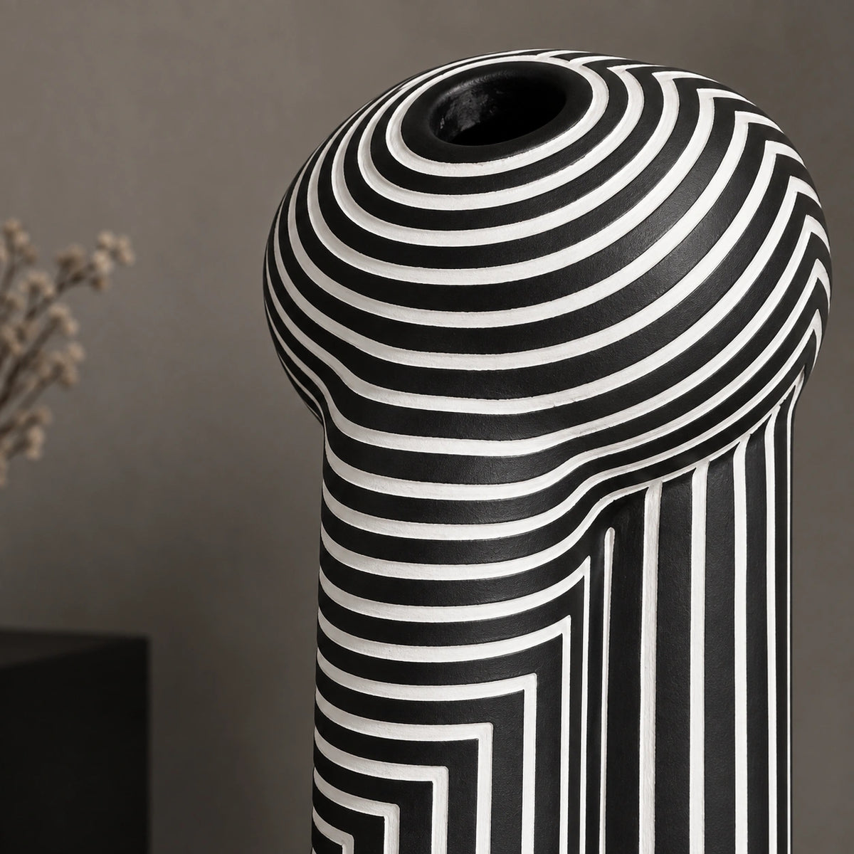 Close-up of a modern black ceramic vase featuring bold white spiral and geometric maze-like stripes, with a rounded sculptural top and opening.