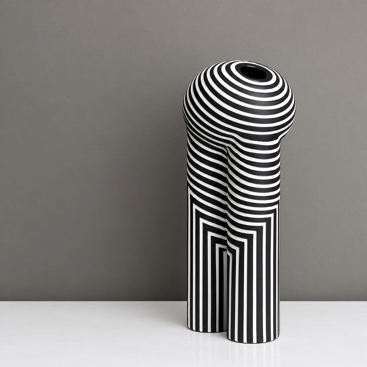 Tall black decorative vase with white geometric striped patterns and yellow flowers, displayed on a modern white console table in a warm contemporary interior