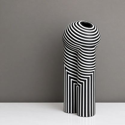 Tall black decorative vase with white geometric striped patterns and yellow flowers, displayed on a modern white console table in a warm contemporary interior