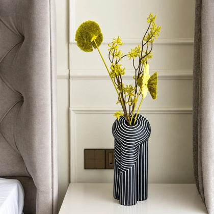 Tall black decorative vase with white geometric striped patterns and yellow flowers, displayed on a modern white console table in a warm contemporary interior
