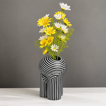 Black and white striped decorative vase with yellow and white flowers on a white tabletop