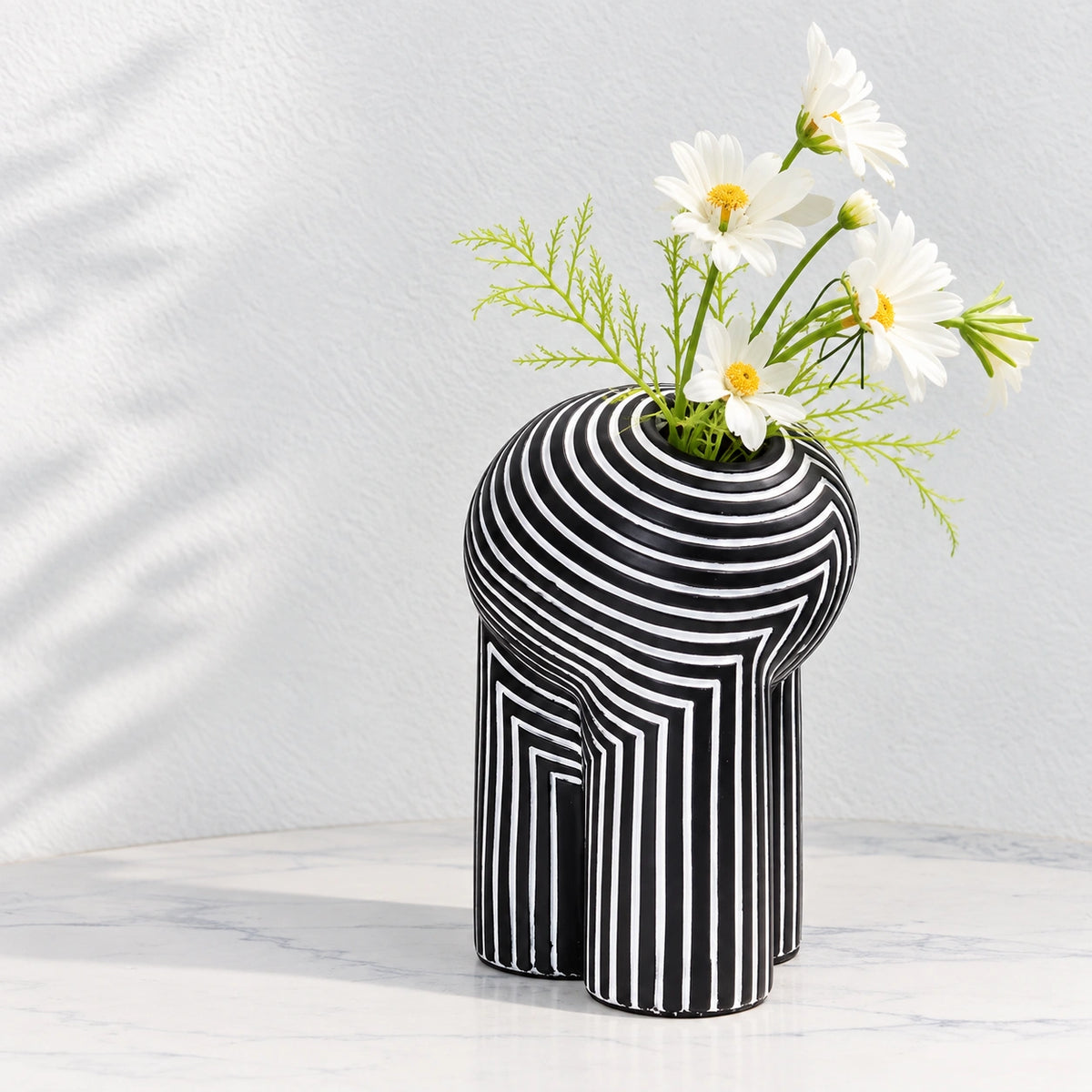 Black and white striped decorative vase with yellow and white flowers on a white tabletop