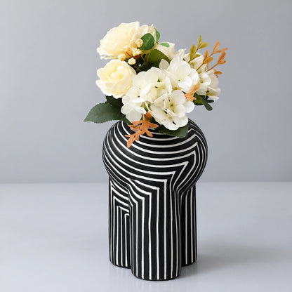 Black and white striped decorative vase with yellow and white flowers on a white tabletop